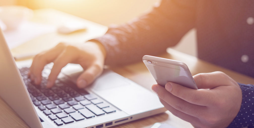 a person holding an iphone and typing on the computer